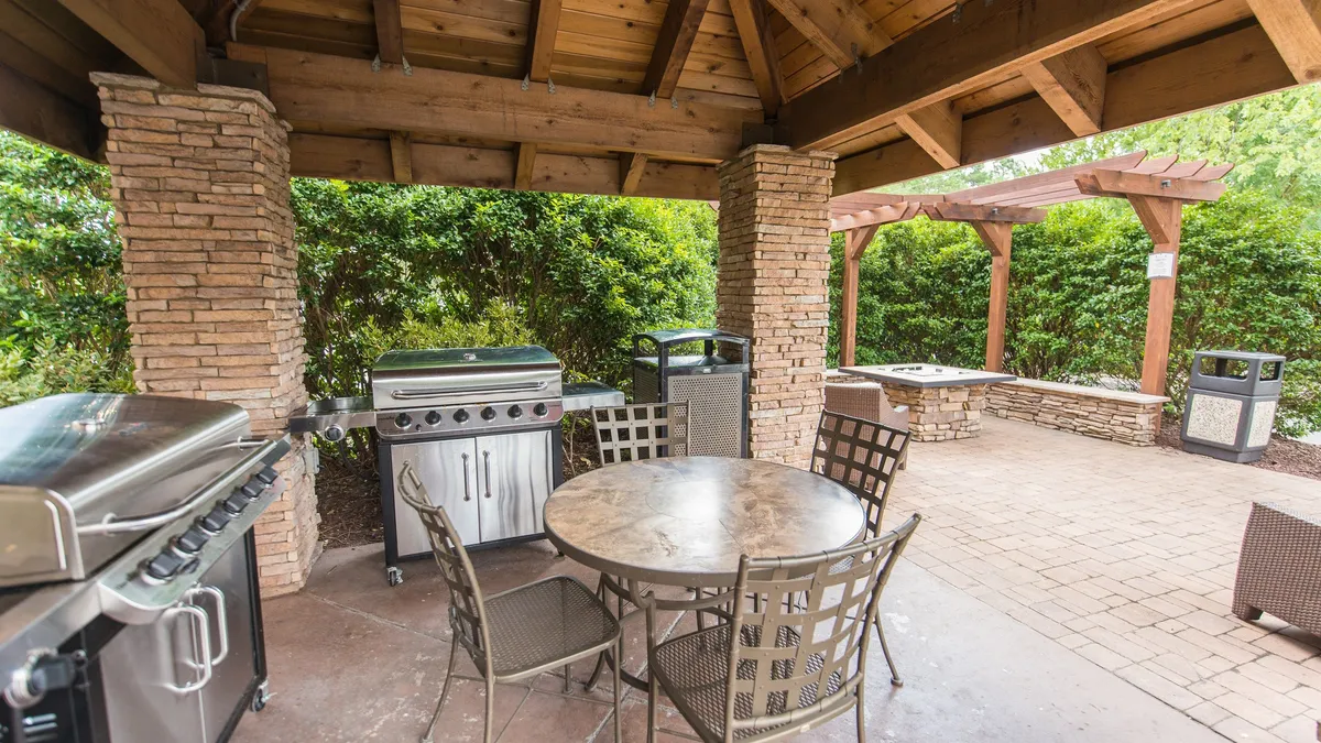 An outdoor grilling station equipped for barbecuing, with a nearby dining table set amidst landscaped greenery. The space is lively yet relaxed, ideal for social gatherings and enjoying meals outdoors.
