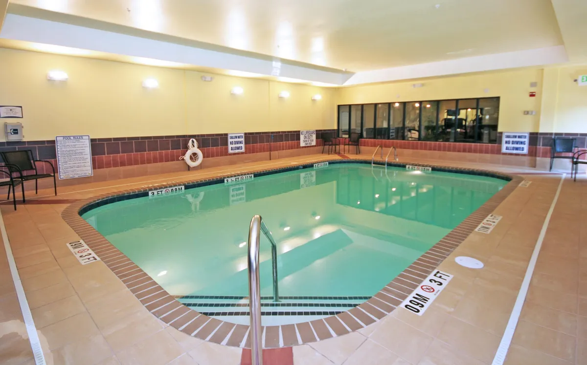 A serene hotel swimming pool area is showcased under natural daylight, with inviting blue water, a stainless steel pool ladder, and cozy seating arranged around the deck. The setting exudes a relaxing ambiance, perfect for guests looking to unwind after a day of exploring or to enjoy some leisure time together.