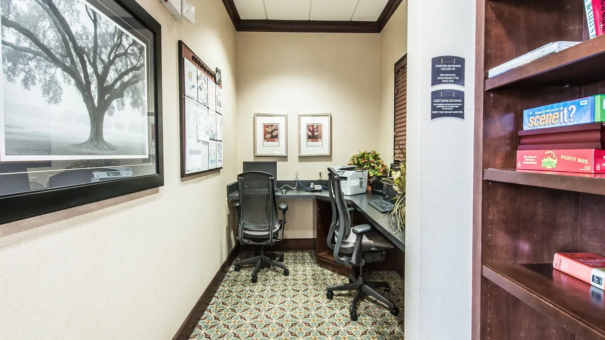 A modern business center setup with a work desk, computer, bookshelf, stylish artwork, and a touch of greenery. The atmosphere is quiet and focused, suggesting a productive environment for remote work, studying, or collaboration.