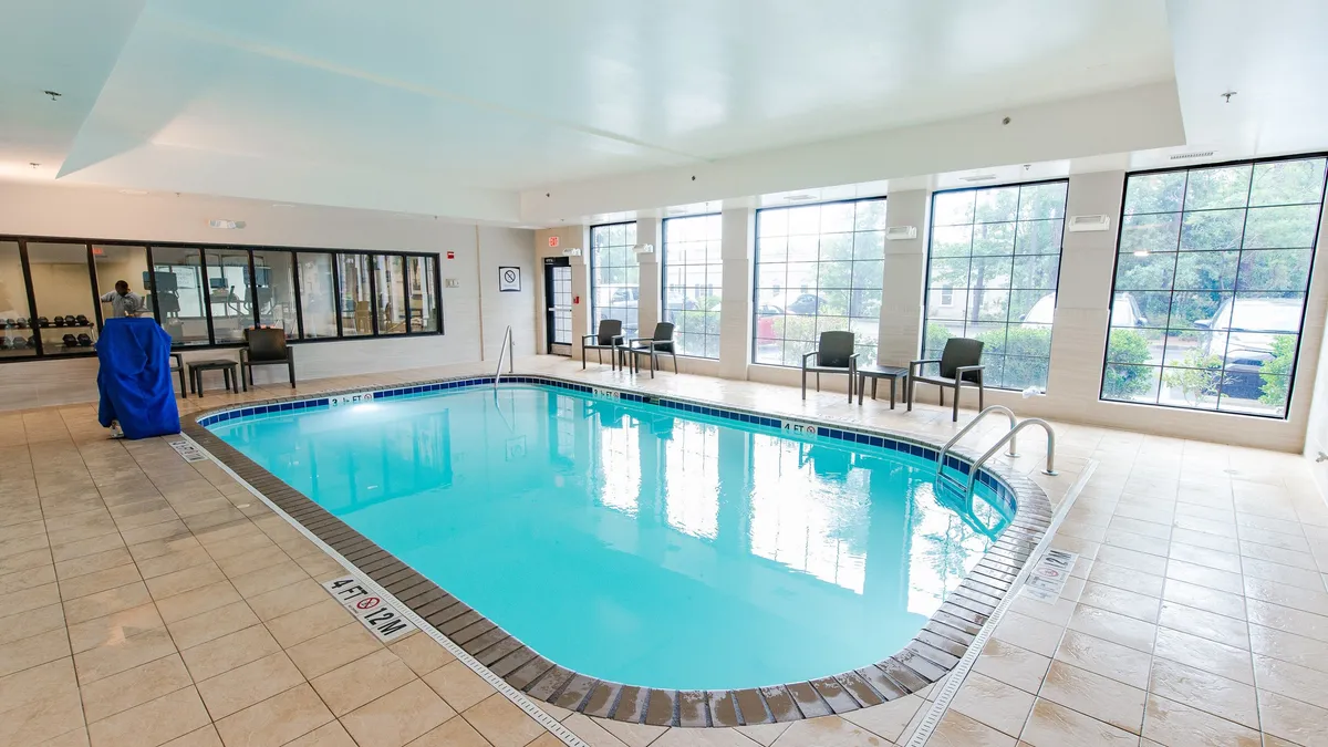 A bright, inviting indoor swimming pool area, featuring large windows that let in natural light, a seating area for relaxation or socializing, and ample space for both swimming and lounging. The serene mood suggests a perfect spot for morning laps or unwinding with family and friends after a busy day.