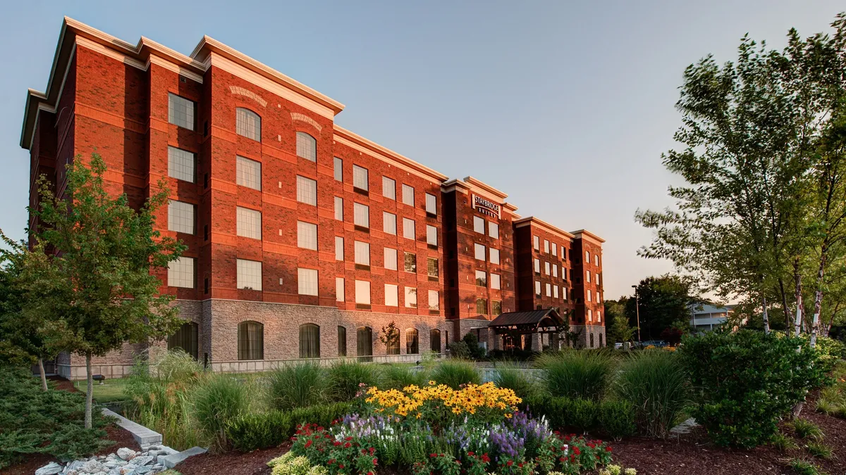 This exterior shot shows the welcoming brick facade of the property, enhanced by colorful flower beds and a prominent entrance canopy. The landscaped gardens create an inviting atmosphere, hinting at a vibrant arrival experience and easy access to nearby attractions.